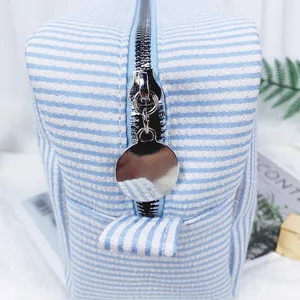 Nahaufnahme einer blau gestreiften Seersucker-Kosmetiktasche mit silbernem Metallreißverschluss