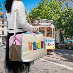 Large travel bag with colorful 'vacay' embroidery shown in a European street setting.