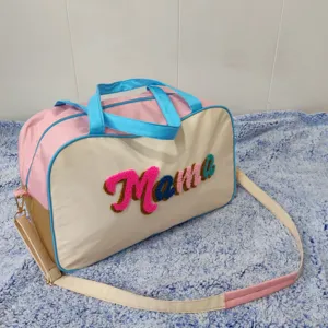 Close-up detail of a large pastel travel bag featuring colorful chenille Mama embroidery.