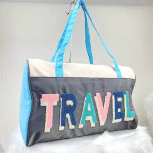 Detail of travel bag with colorful embroidered TRAVEL lettering on grey fabric.