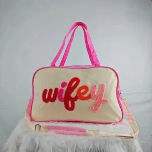 Detailed view of cream travel bag with colorful fuzzy 'wifey' embroidery and pink accents