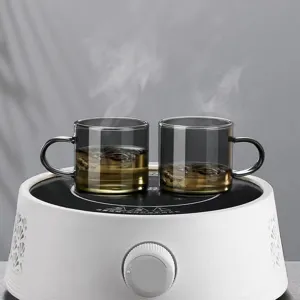 Elegant smoke gray heat-resistant glass teacups with handles on white electric heater base