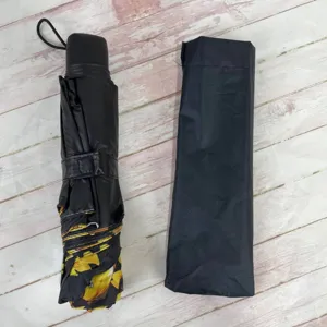 Close-up of a folded manual sun umbrella with sunflower print and a black protective sleeve