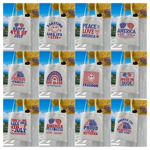 Selection of white canvas tote bags with patriotic 4th of July slogans and graphics.
