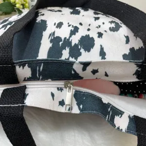 Detail of durable metal zipper on a black and white cow print canvas tote bag
