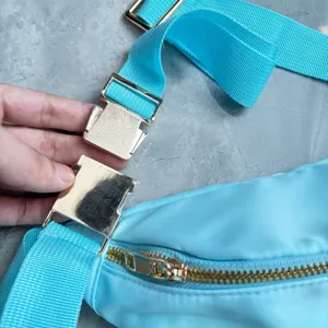 Close-up of gold metal buckle and blue strap on a crossbody travel bag.