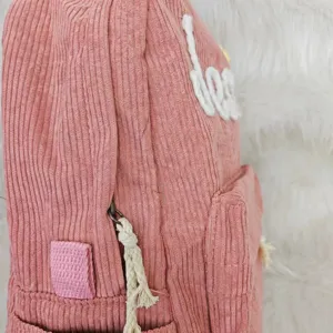 Close-up of pink corduroy backpack featuring white plush embroidered name and rope pull