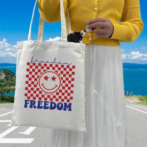 Close-up of a white canvas tote bag with red checkered pattern and star-eyed smiley design
