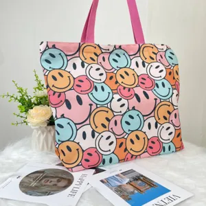Large canvas tote bag featuring a colorful all-over smiley face print with pink handles.