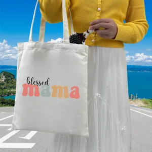 Detail view of white canvas tote bag with 'blessed mama' print used by a person outdoors.