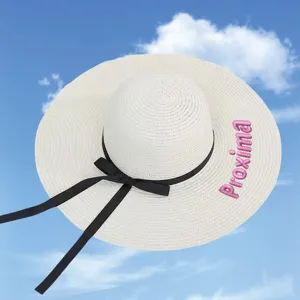 White straw sun hat with black bow and pink custom embroidery against a blue sky.