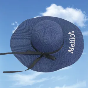 Close-up of blue straw sun hat with black bow and embroidered Melilot lettering