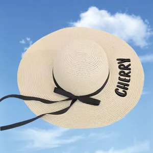 Straw sun hat detail with elegant black bow and CHERRY embroidery on the wide brim