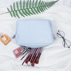 Gestreifte Seersucker-Kosmetiktasche mit Pinseln auf weichem weißem Hintergrund.