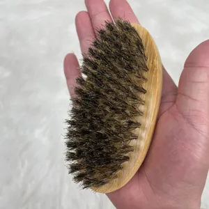 Cepillo de bambú ovalado para barba con cerdas naturales de jabalí en la mano