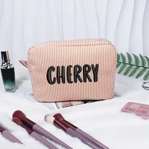 Detailaufnahme einer orange gestreiften Seersucker Kosmetiktasche mit CHERRY Stickerei