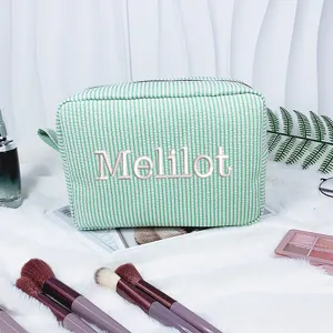 Nahaufnahme einer grün gestreiften Seersucker-Kosmetiktasche mit Melilot-Stickerei
