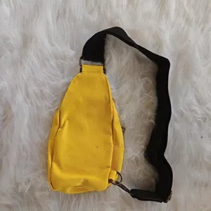 Close-up of vibrant yellow canvas sling bag with black adjustable strap and hardware