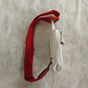 Side view of white canvas crossbody bag with red strap on white faux fur background