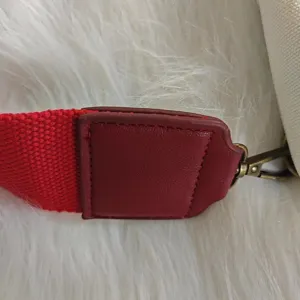 Detailed view of red woven webbing strap with vintage bronze clasp for canvas sling bag