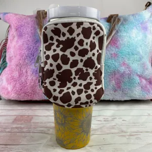 Cow print water bottle pouch for 40oz tumblers shown on a sunflower pattern cup