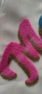 Macro view of pink and brown chenille embroidery letter detail on travel bag fabric