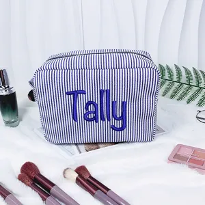 Detailansicht der blau gestreiften Seersucker-Kosmetiktasche mit dem Namen Tally bestickt