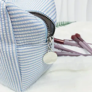 Nahaufnahme einer gestreiften Seersucker-Kosmetiktasche mit silbernem Reißverschluss-Detail.