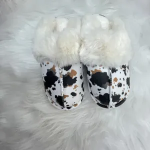 Close-up of stylish cow print slippers featuring thick white faux fur lining and trim.