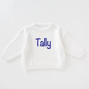 Detailed view of white knitted kids sweater with blue 'Tally' name embroidery
