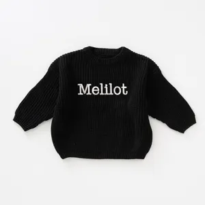 Detailed view of a black chunky knitted sweater with white Melilot embroidery on the front.