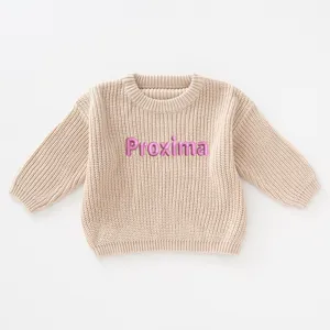 Close-up of beige knitted girl's sweater with pink custom embroidered name Proxima detail
