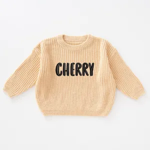 Close-up view of beige knitted sweater featuring black 'CHERRY' embroidery detail