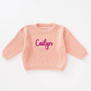 Close-up detail of a pink knitted baby sweater featuring custom Cailyn name embroidery