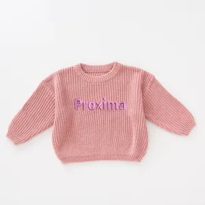 Close-up detail of a soft pink girls' knitted sweater featuring purple 'Proxima' embroidery.