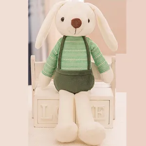 Close-up of a cute plush white rabbit doll wearing green striped clothes on a wooden stool.