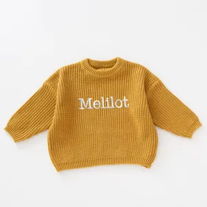 Close-up of yellow knitted sweater for kids with custom Melilot letter embroidery detail.