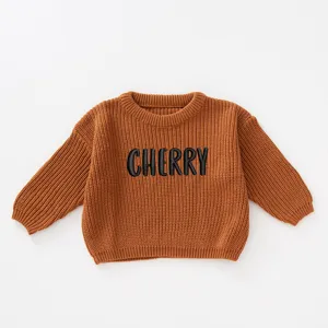 Detail of a brown knitted baby sweater with black CHERRY embroidery