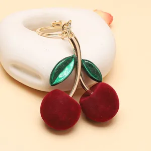 Gros plan d'un porte-clés cerise floqué rouge avec feuilles pailletées et anneau doré