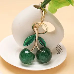 Vue détaillée d'un porte-clés cerise vert pailleté avec une chaîne en métal doré.