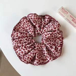 Détail en gros plan d'un chouchou rose motif léopard cœur avec bord volanté, attache cheveux.