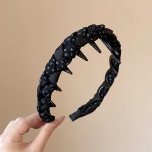 Vista detallada de una diadema trenzada negra con dientes y patrón floral, accesorio para el pelo.