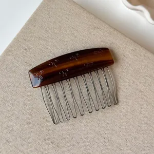 Dettaglio di un pettine per capelli in acetato con motivo tartarugato e fiocchi incisi.