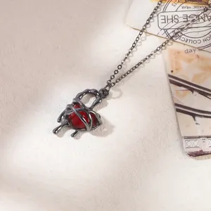 Macro detail of a gothic red heart necklace featuring black liquid metal cage design