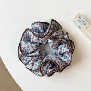 Vue en gros plan de chouchou en satin à motif léopard bleu avec bordure marron.