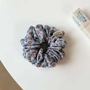 Gros plan d'un chouchou à cheveux en satin à motif léopard bleu et marron avec étiquette.