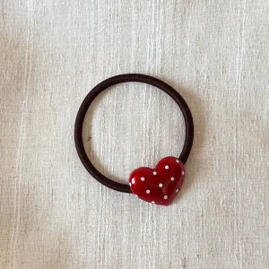 Detailed closeup of a dark brown hair tie with a cute red white-dotted heart charm.