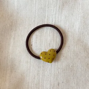 Close-up detail of dark brown hair tie with glossy olive green polka dot heart pendant accessory.