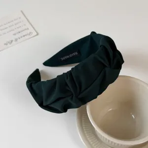 Detailed view of the dark green pleated fabric headband, showcasing fine texture and handmade label.