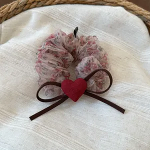 Primo piano di un elastico per capelli floreale con cuore rosso e nastro marrone.